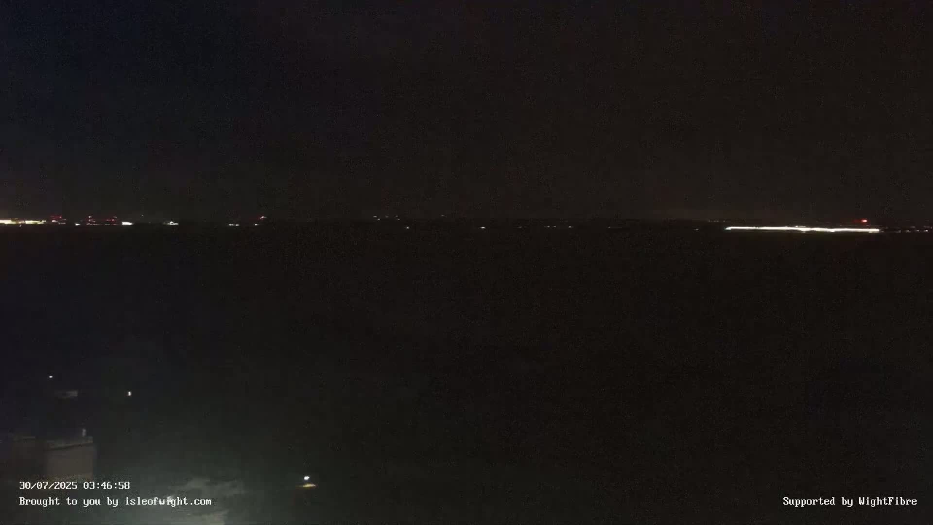 A coastal town with a long pier extends into a calm, overcast body of water, with a distant shoreline visible on the horizon.