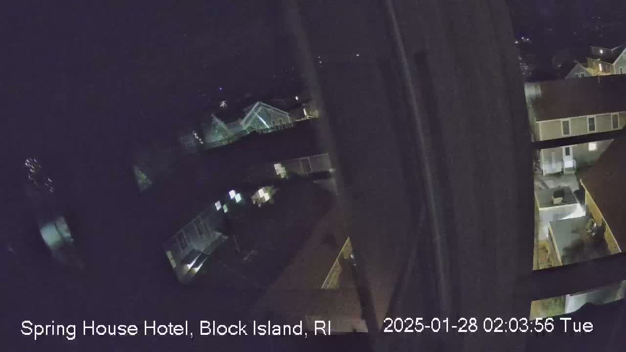 A nighttime, high-angle view from a window shows several buildings with dimly lit windows and an exterior courtyard.