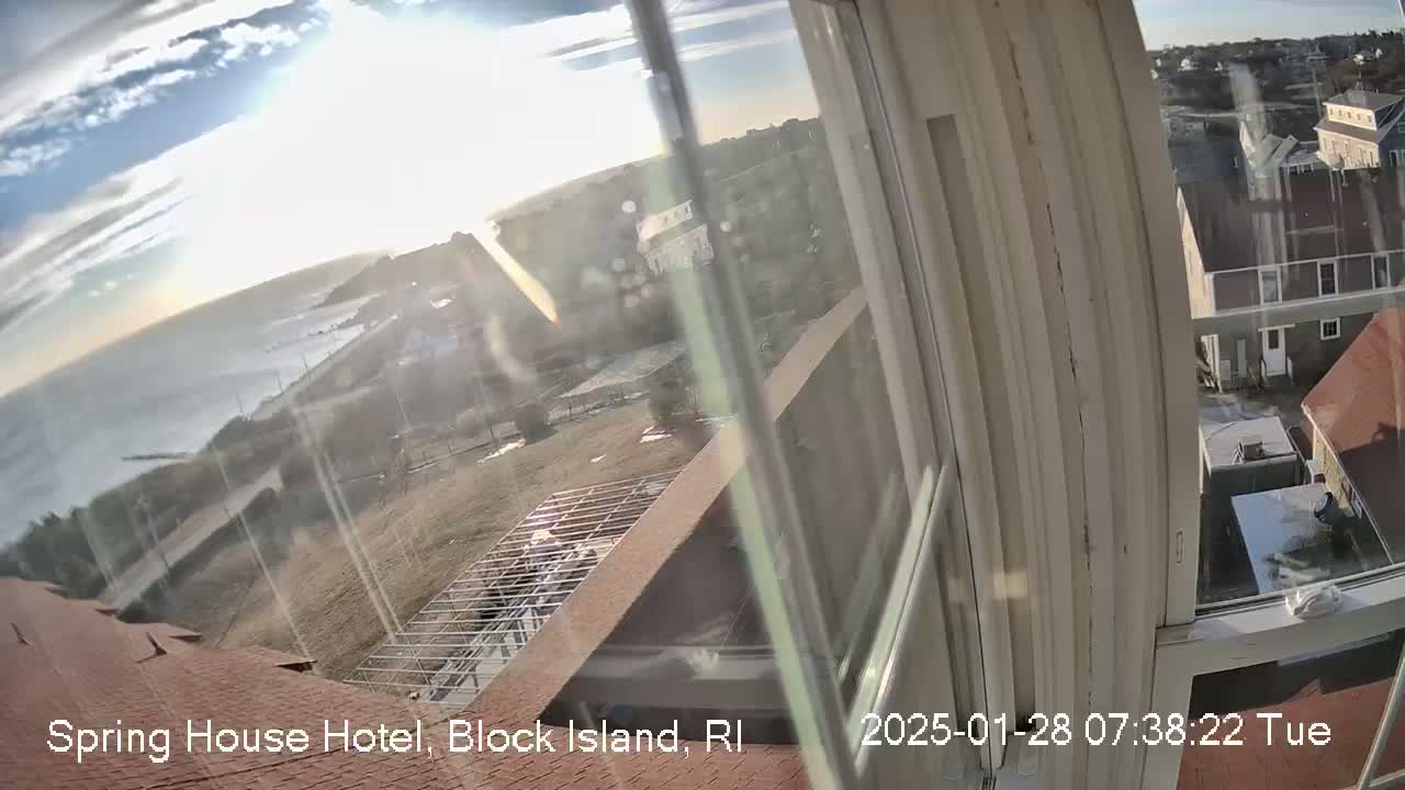 A partly sunny view of the ocean and buildings from a window, showing a mostly clear sky.