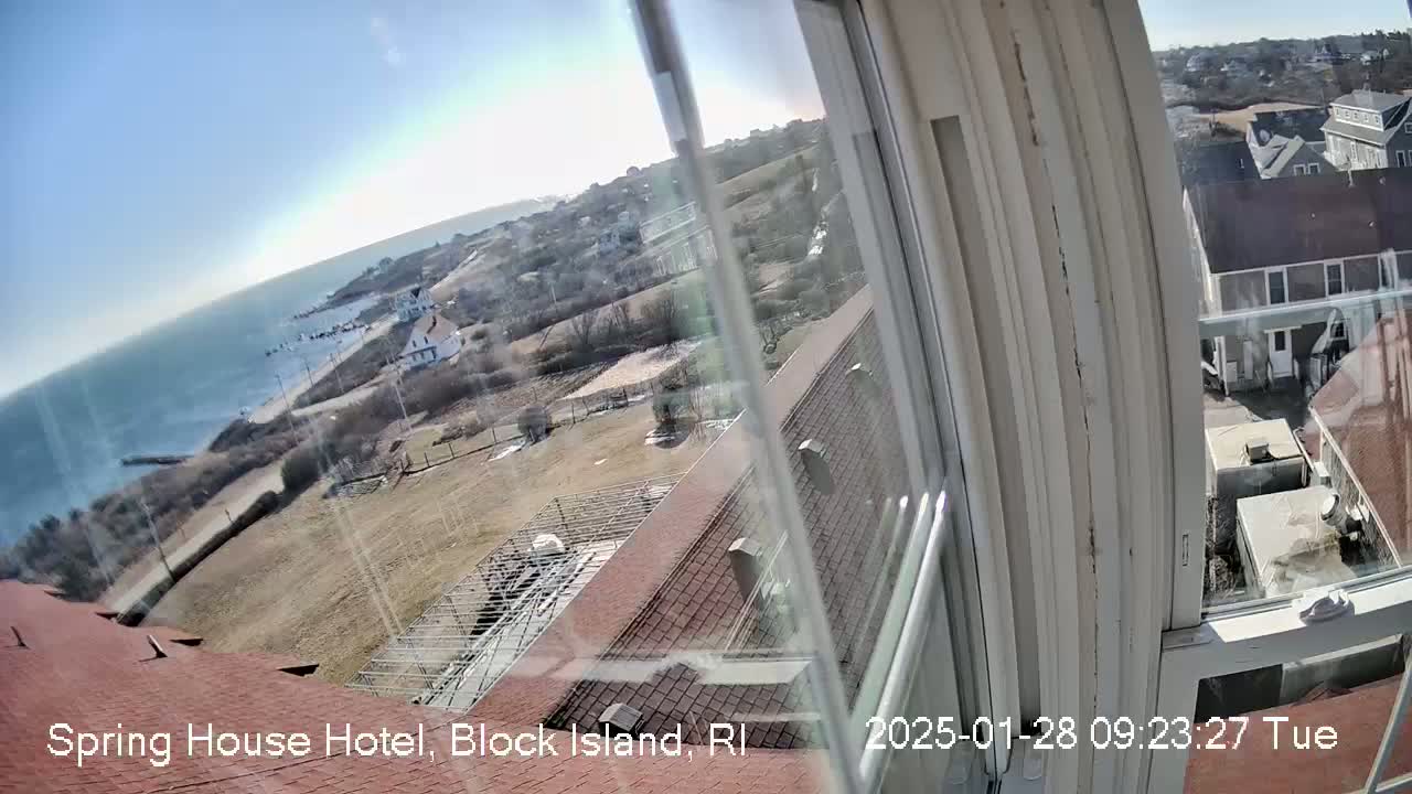 A view from a window shows a sunny, coastal scene with buildings, ocean, and barren winter landscape.