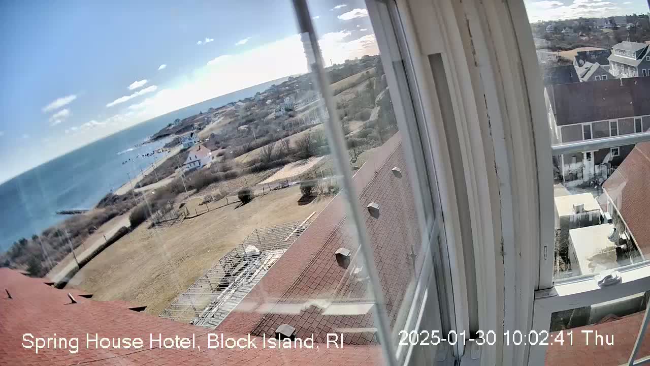 A view from a window shows a mostly sunny day overlooking a coastline, a residential area, and part of a red roof.