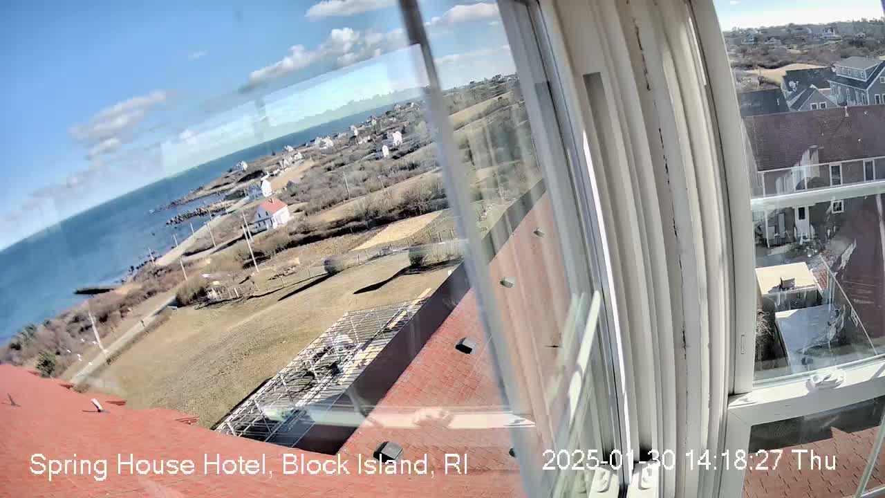 A view from a window shows a coastal town on a sunny day, with a body of water visible in the distance.