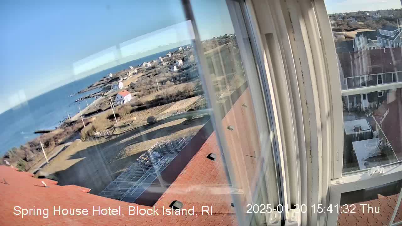 A window view shows a coastal scene on a sunny day, encompassing a body of water, a shoreline with buildings, and a section of red roof.