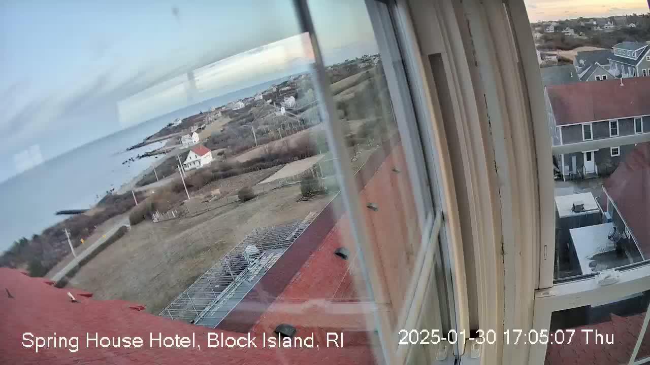 A view from a window shows a coastal town on a partly cloudy day, with the ocean visible in the distance.