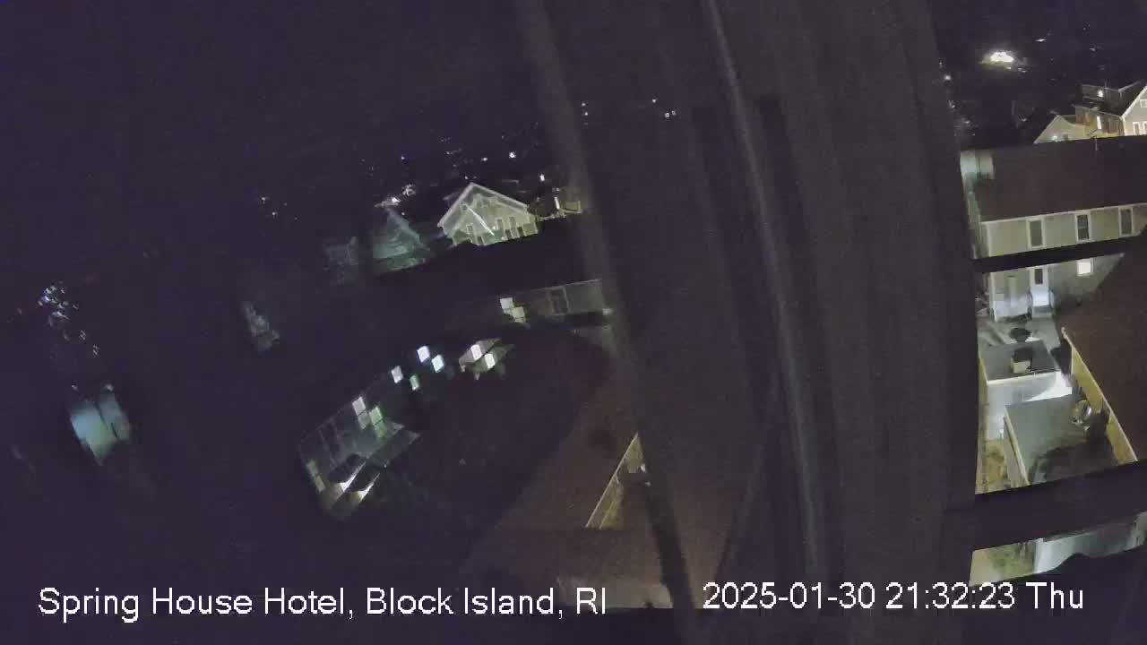 A nighttime, high-angle view from a window shows a dark residential area with dimly lit buildings.