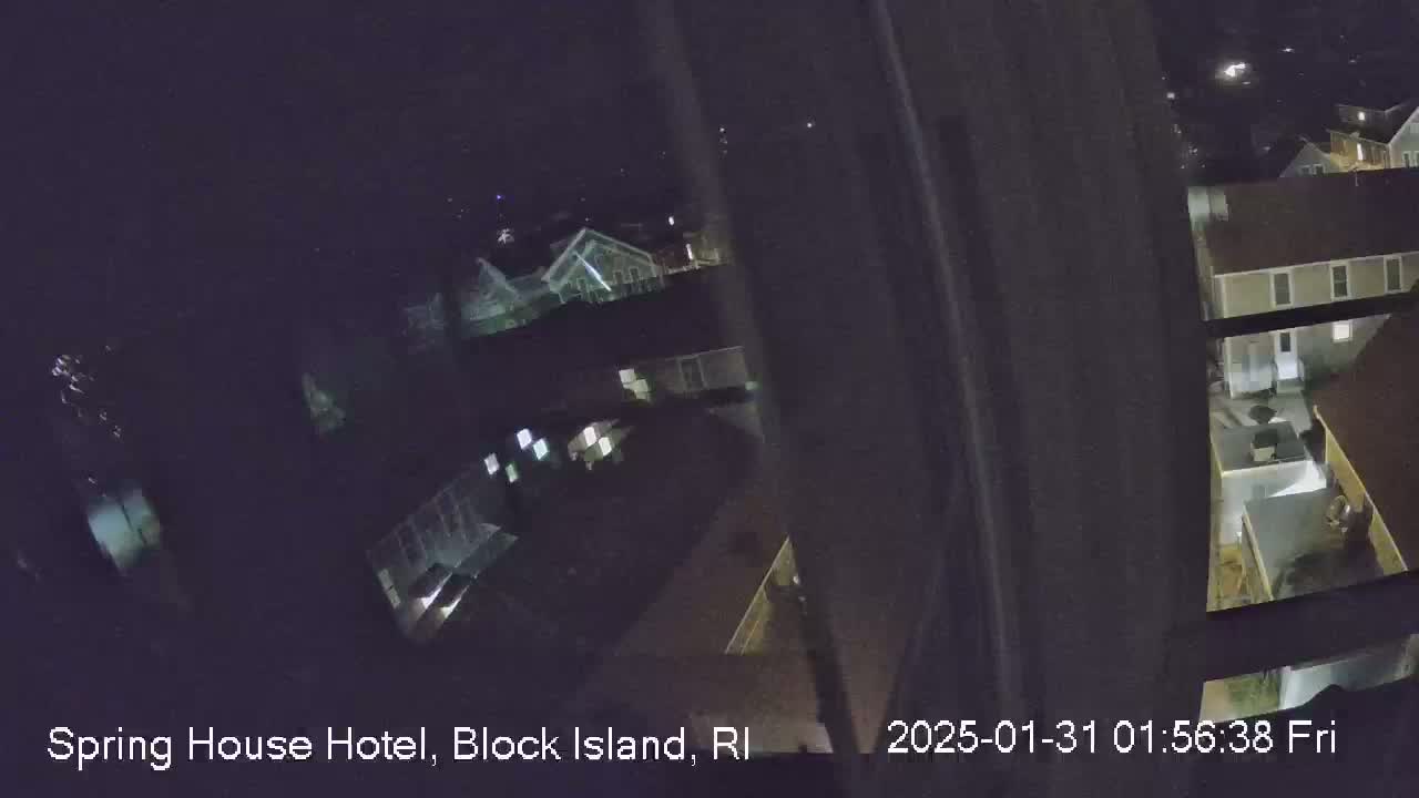 A nighttime, high-angle view from a window shows a cluster of buildings illuminated by artificial light.