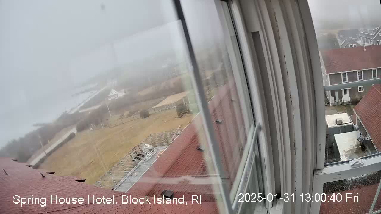 A foggy view from a window shows a red-roofed building, a yard, and other buildings in the distance.