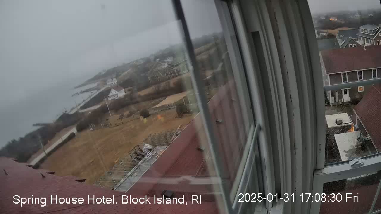 A view from a window shows a coastal town on an overcast day, with buildings and a body of water visible in the distance.