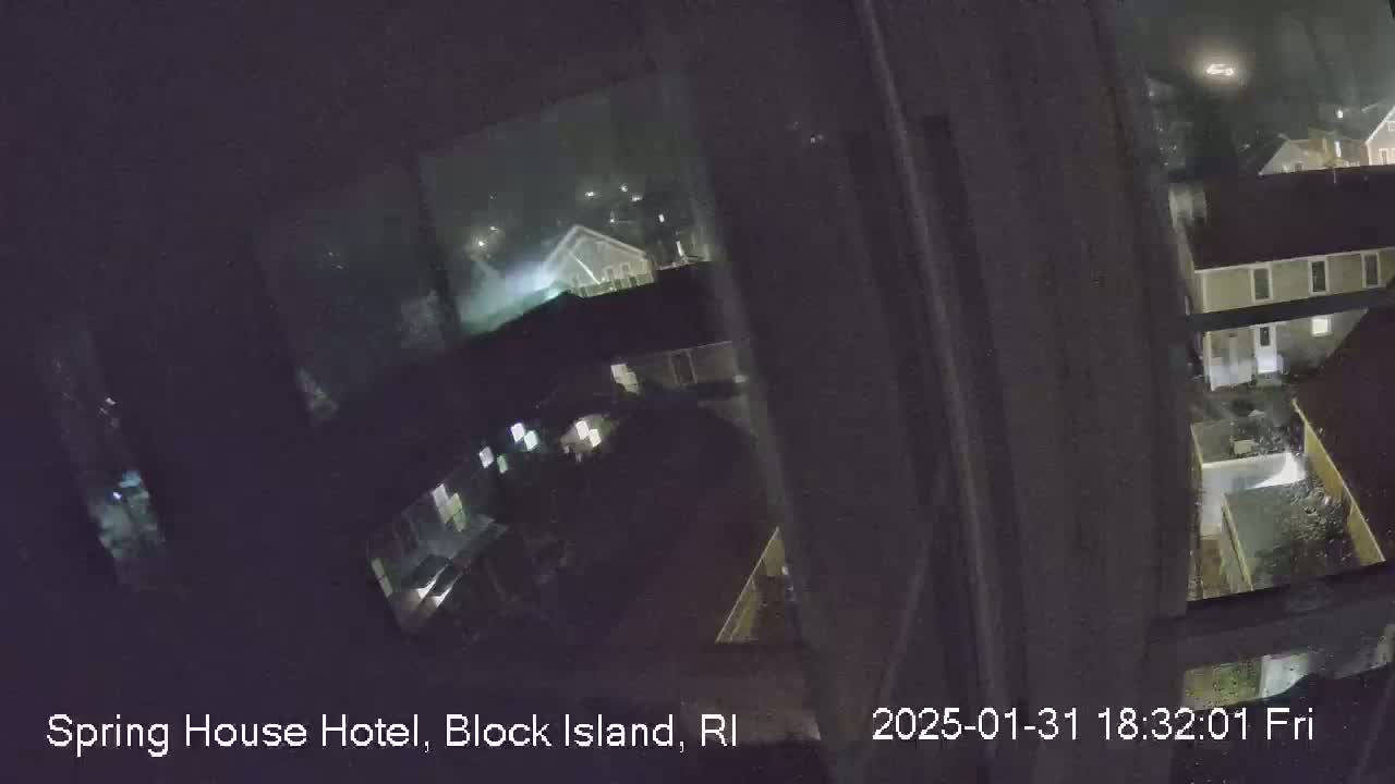 A nighttime view from a window shows rain falling on a cluster of buildings.