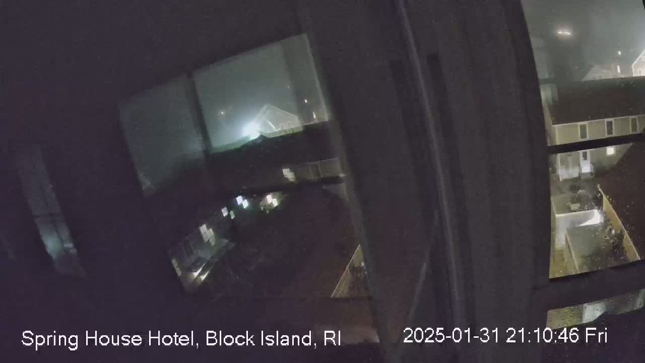 A nighttime view from a window shows rain falling on buildings and a courtyard.