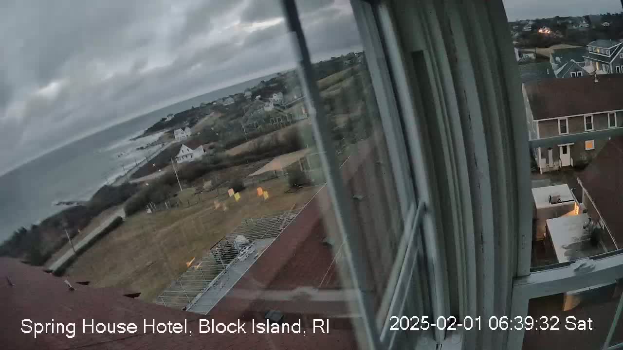A view from a window shows a cloudy, overcast day over a coastal town with a body of water in the background.