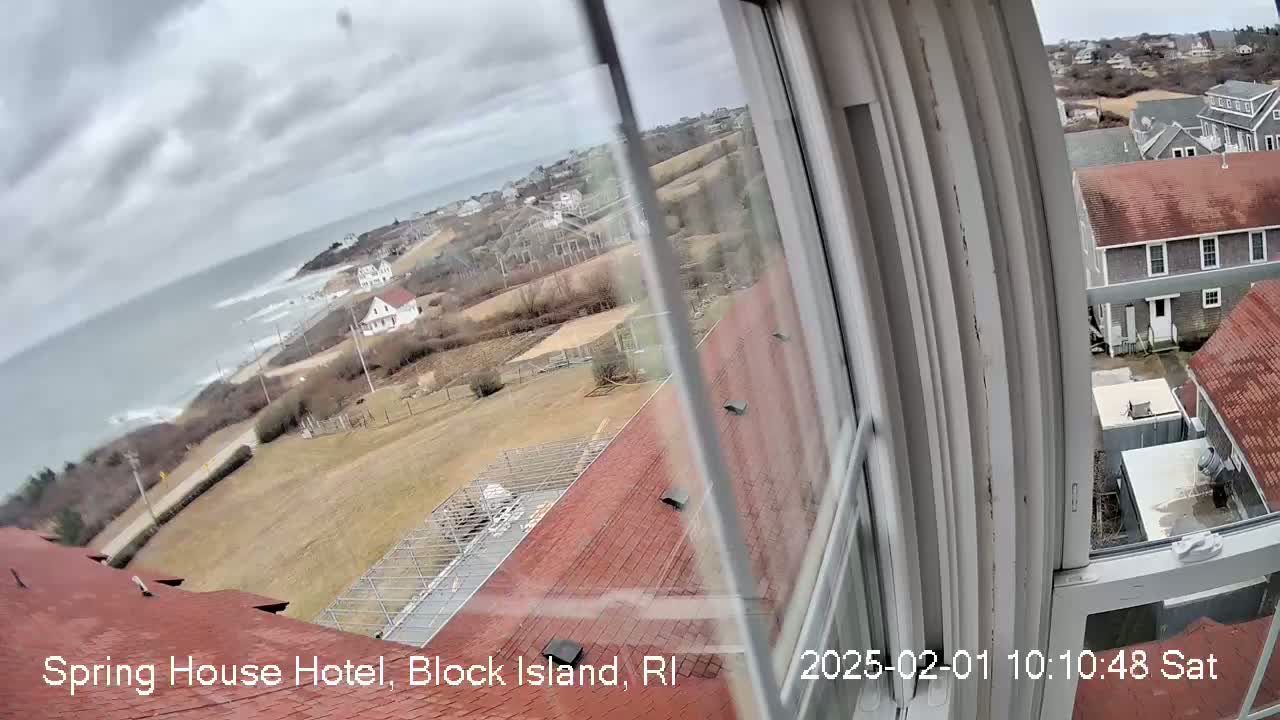 A view from a window shows a coastal town under an overcast sky, with a grey sea visible in the distance.