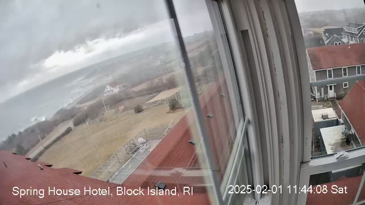 A view from a window shows an overcast day with a stormy ocean, buildings, and a sparsely vegetated landscape.