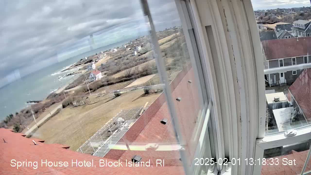 A view from a window shows a cloudy day overlooking a coastline with houses and a partially visible ocean.
