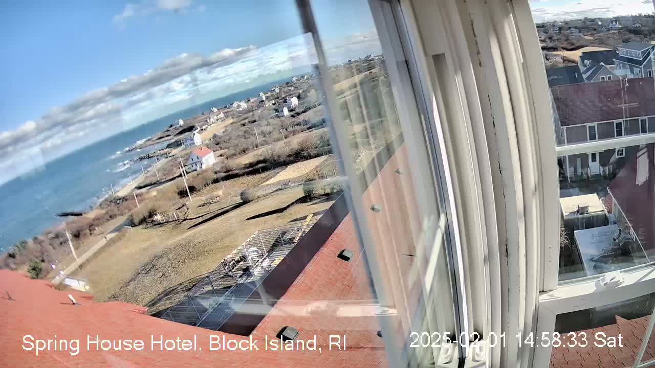 A partly cloudy day's view of a coastal town and ocean seen from a window, with rooftops and some construction visible in the foreground.