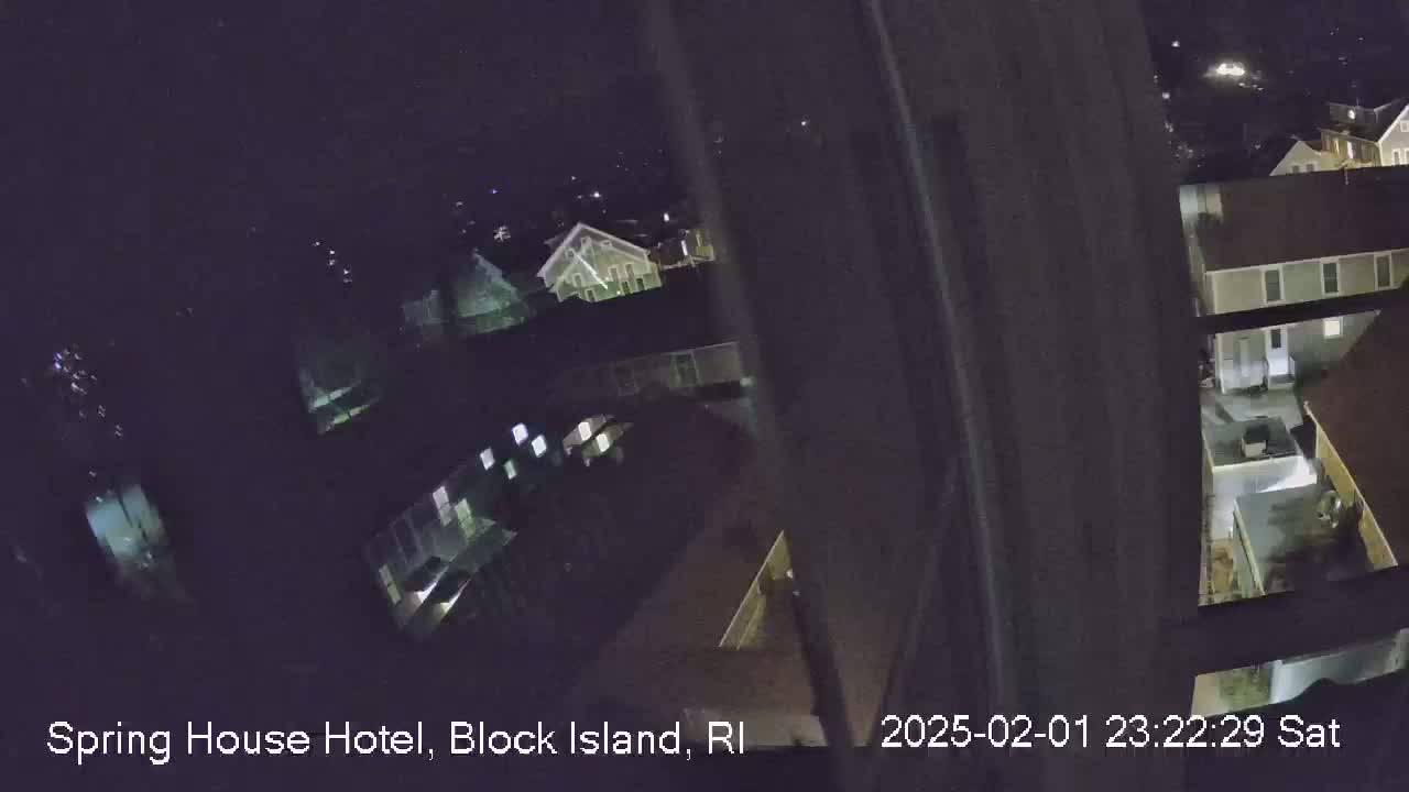 A nighttime, high-angle view shows several buildings with illuminated windows, seen from behind what appears to be a window or screen.