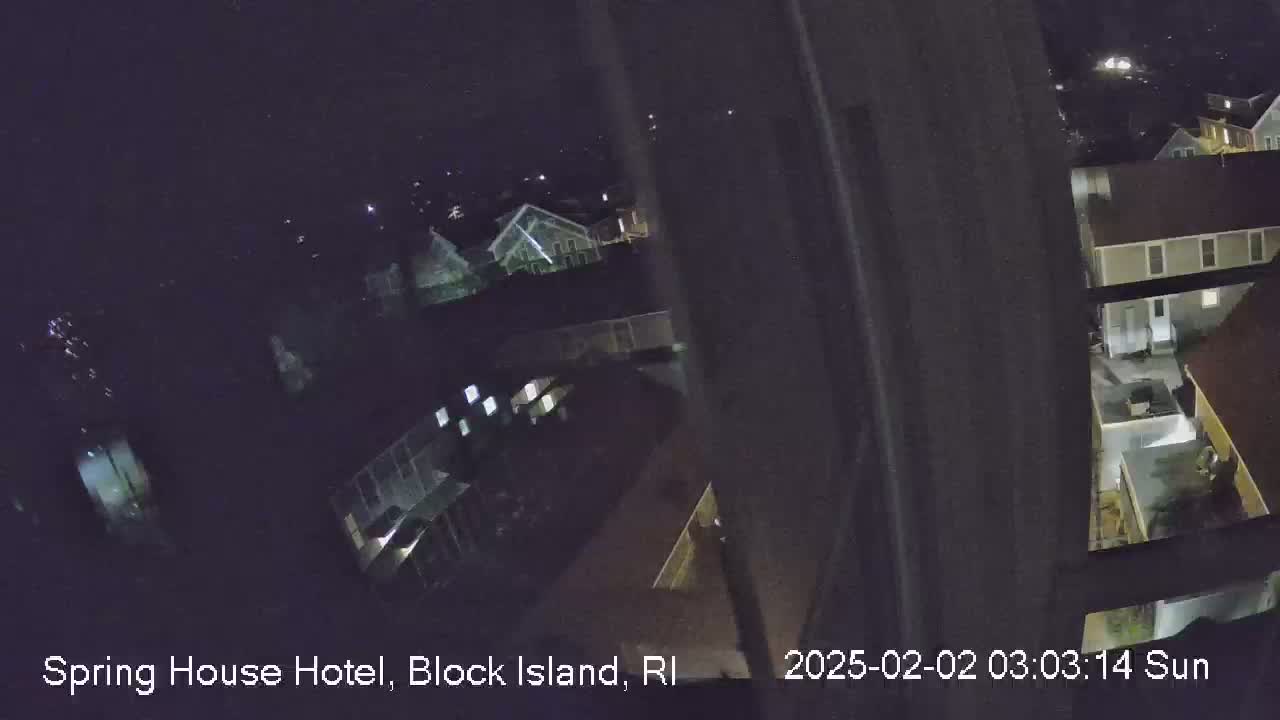 A nighttime, high-angle view shows a residential area with several houses illuminated, under a dark, clear sky.