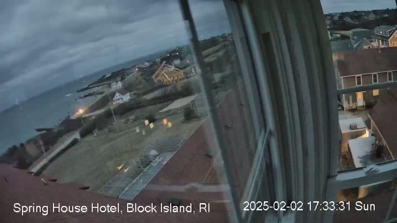 A view from a window shows a coastal town under an overcast sky at dusk, with the ocean visible in the distance.