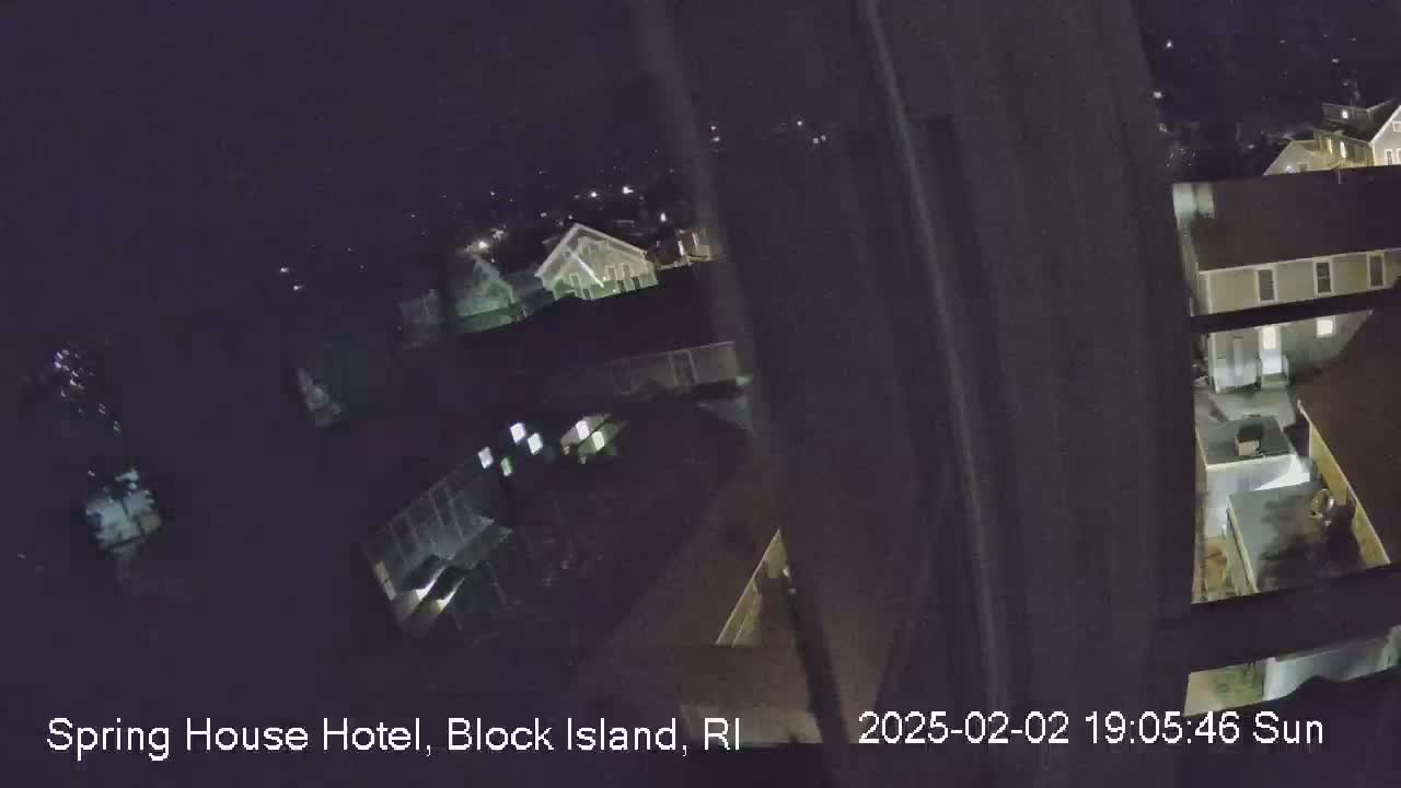 A nighttime, high-angle view from a window shows a cluster of houses with illuminated windows.