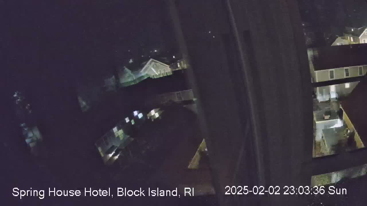 A nighttime, possibly snowy, view from a window shows several houses and yards.