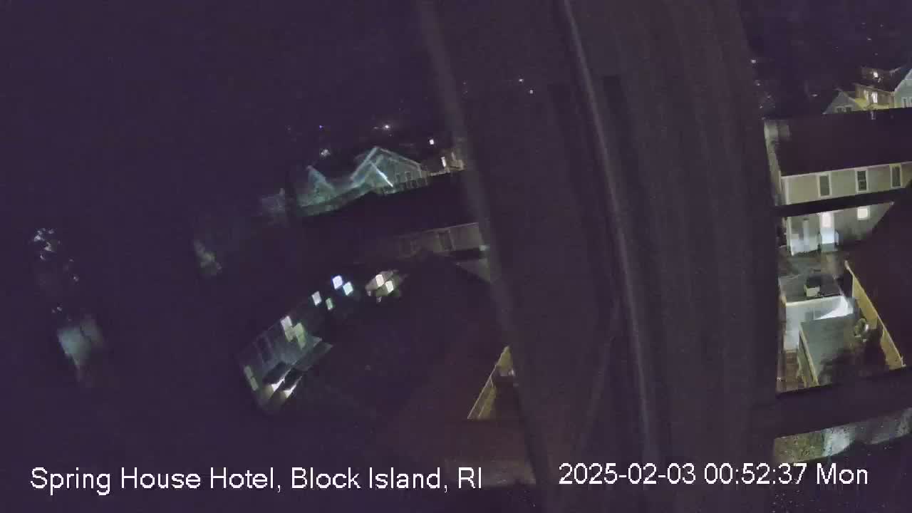 A nighttime, slightly blurry view from a window shows several houses and a small pool, under a dark sky.