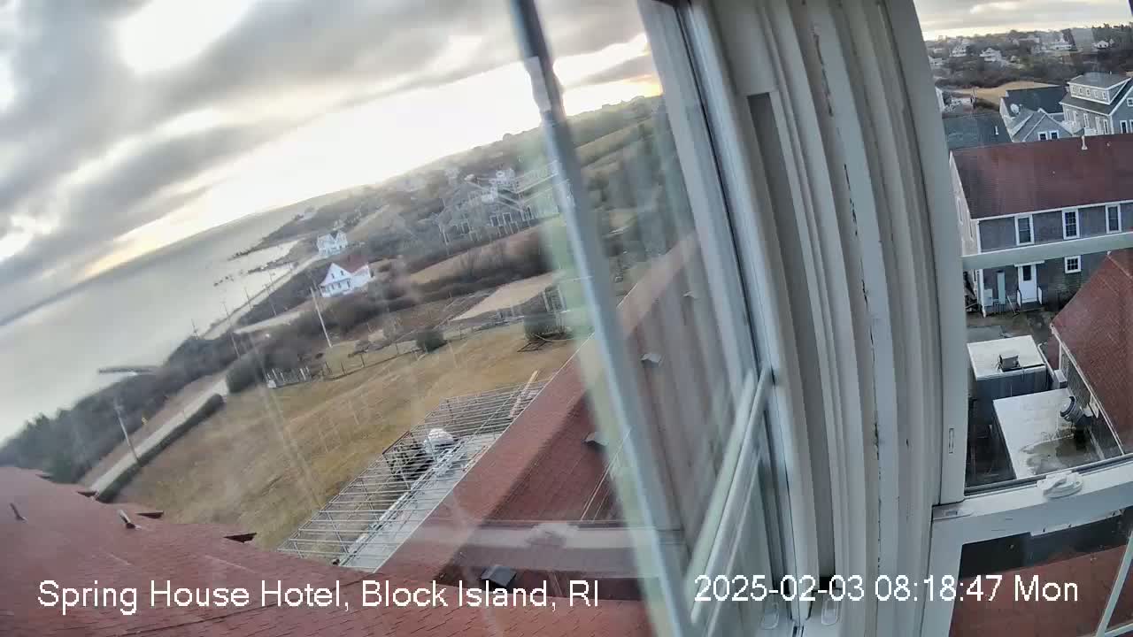 A view from a window shows a coastal town under a cloudy sky, with calm water visible in the distance.