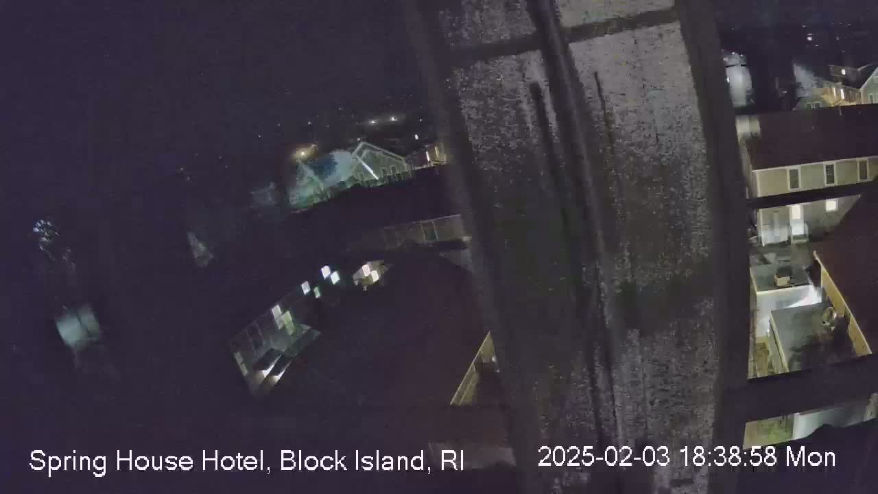 A nighttime, high-angle view of a residential area shows snow-covered ground and buildings with illuminated windows.