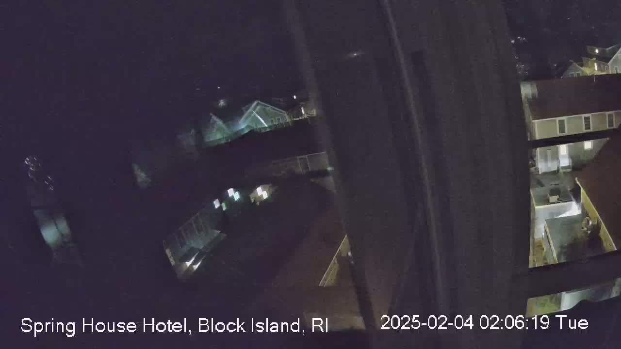 A nighttime, high-angle view shows several buildings with some lights on, partially obscured by a dark window frame.