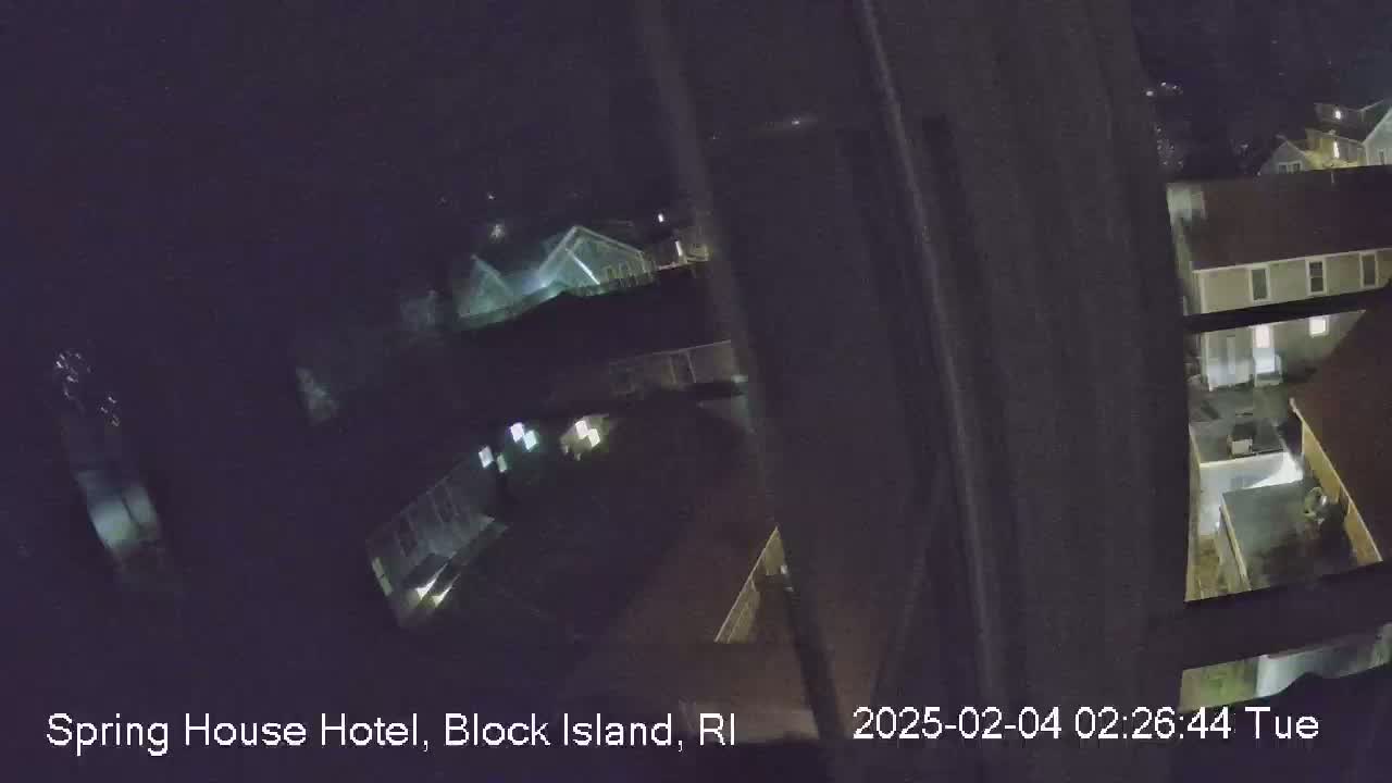 A nighttime, high-angle view shows several houses with some lights on, seen from what appears to be a window.