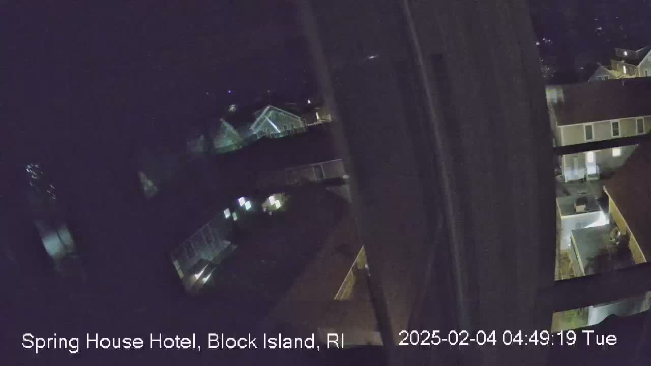 A nighttime, high-angle view shows several buildings with illuminated windows, surrounded by dark grounds.