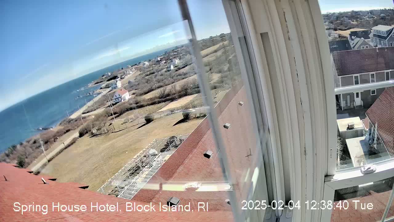A view from a window shows a coastal town on a sunny day, with a body of water visible in the distance.
