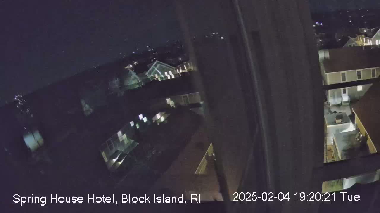 A nighttime, high-angle view shows a cluster of buildings illuminated by interior lights under a clear, dark sky.