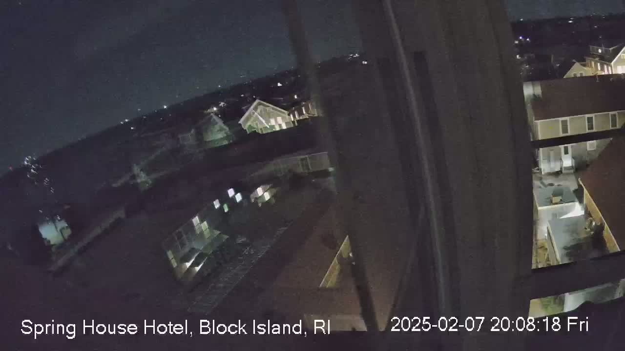 A nighttime, high-angle view from a window shows a cluster of buildings under a clear, dark sky.