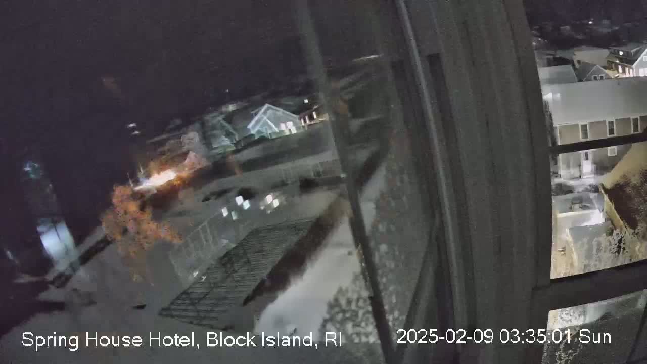A nighttime view through a window shows a snow-covered landscape with buildings and some lights visible.