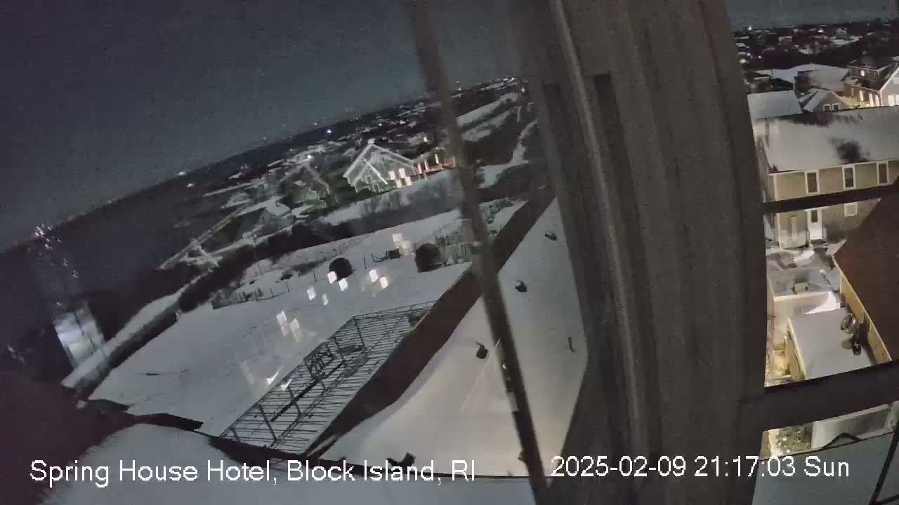 A nighttime view from a window shows a snow-covered landscape with buildings and a metal framework, under a dark, clear sky.