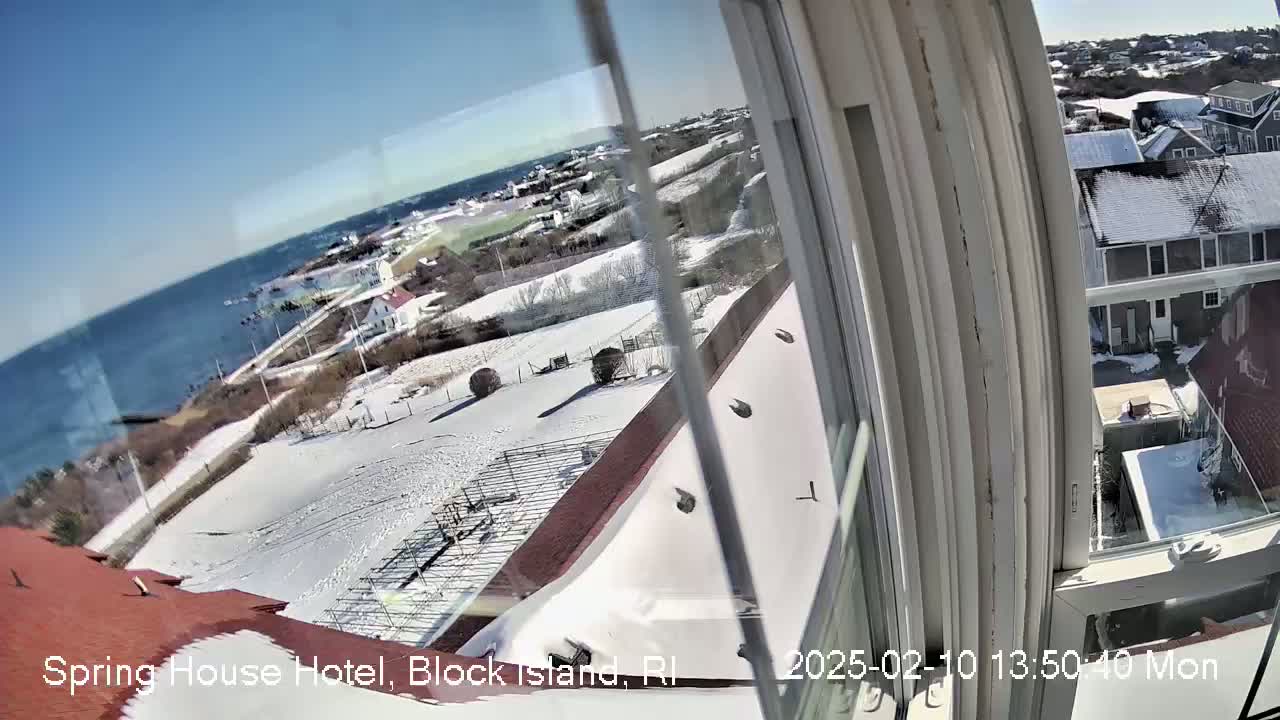 A snow-covered landscape viewed from a window, showing a coastline, buildings, and a clear blue sky.