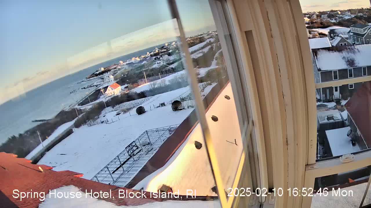 A snow-covered landscape with a coastline and buildings is seen through a window on a partly sunny day.