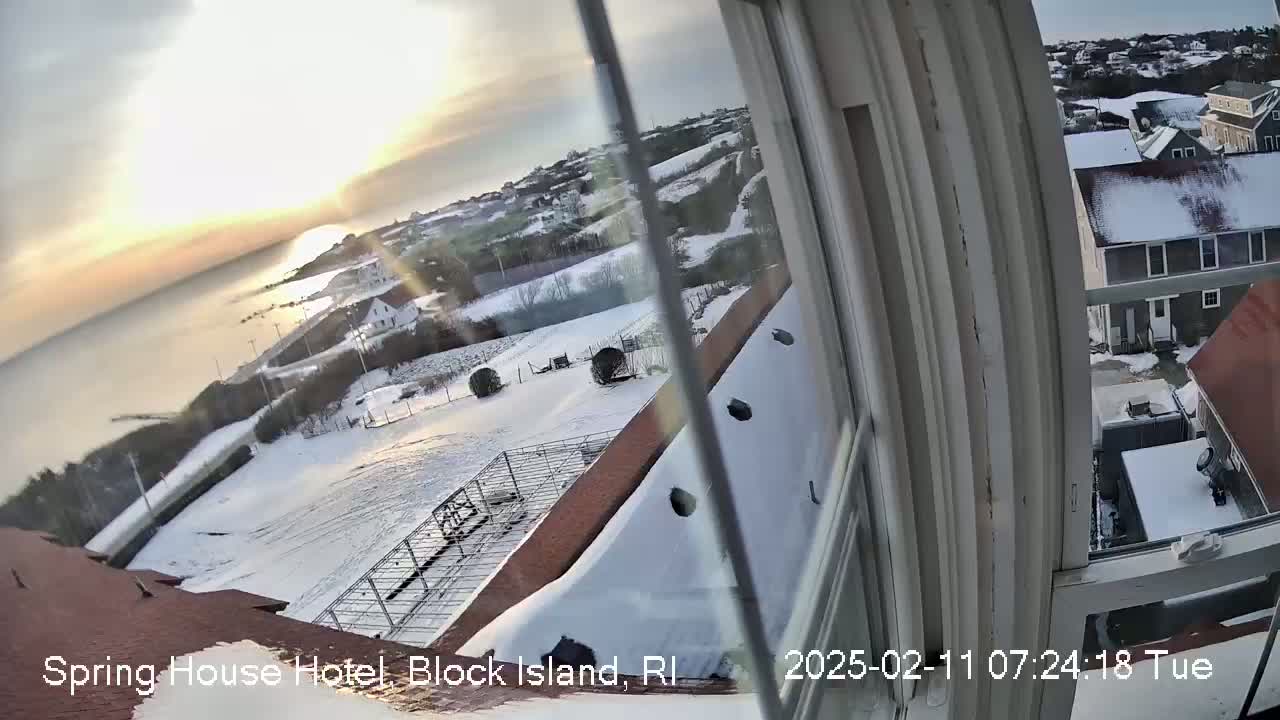 A snow-covered landscape is seen from a window, overlooking a coast at sunrise.