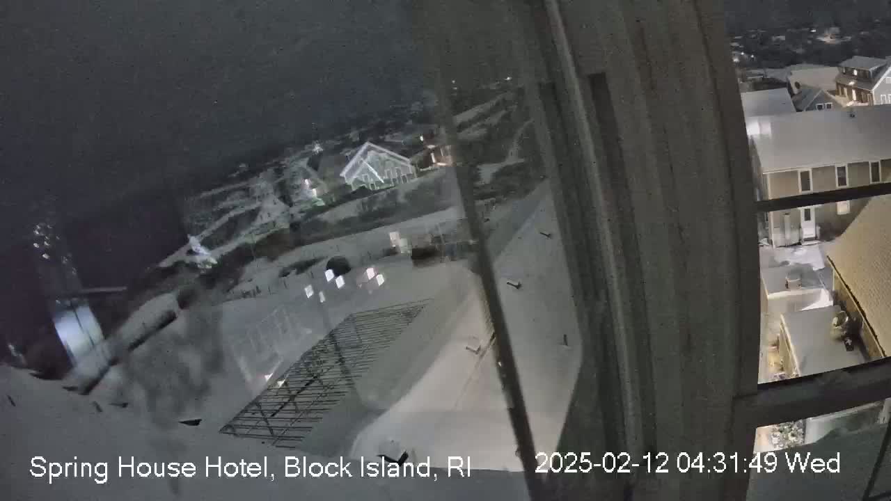 A nighttime, snow-covered view from a window shows a snow-covered landscape with buildings and a metal framework.