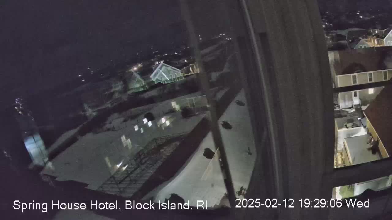 A nighttime, snow-covered view of rooftops and buildings from a high vantage point.