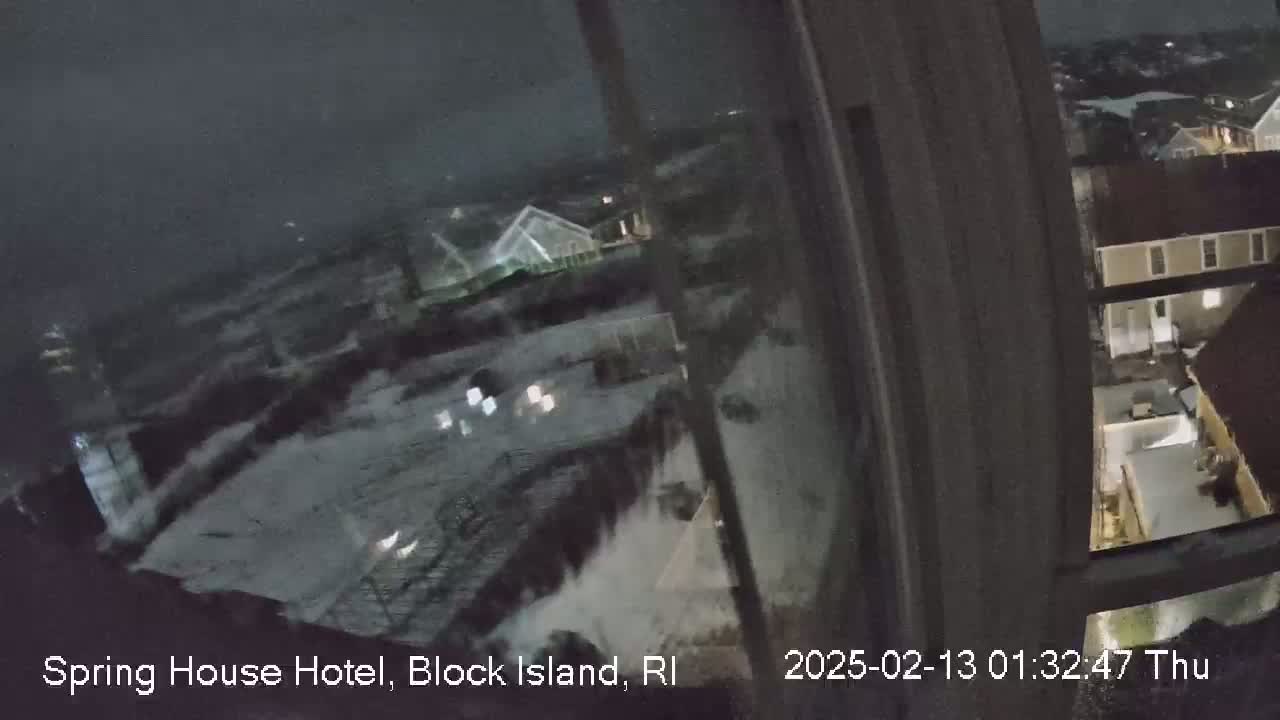 A nighttime view from a window shows snow-covered buildings and a turbulent sea under a dark sky.