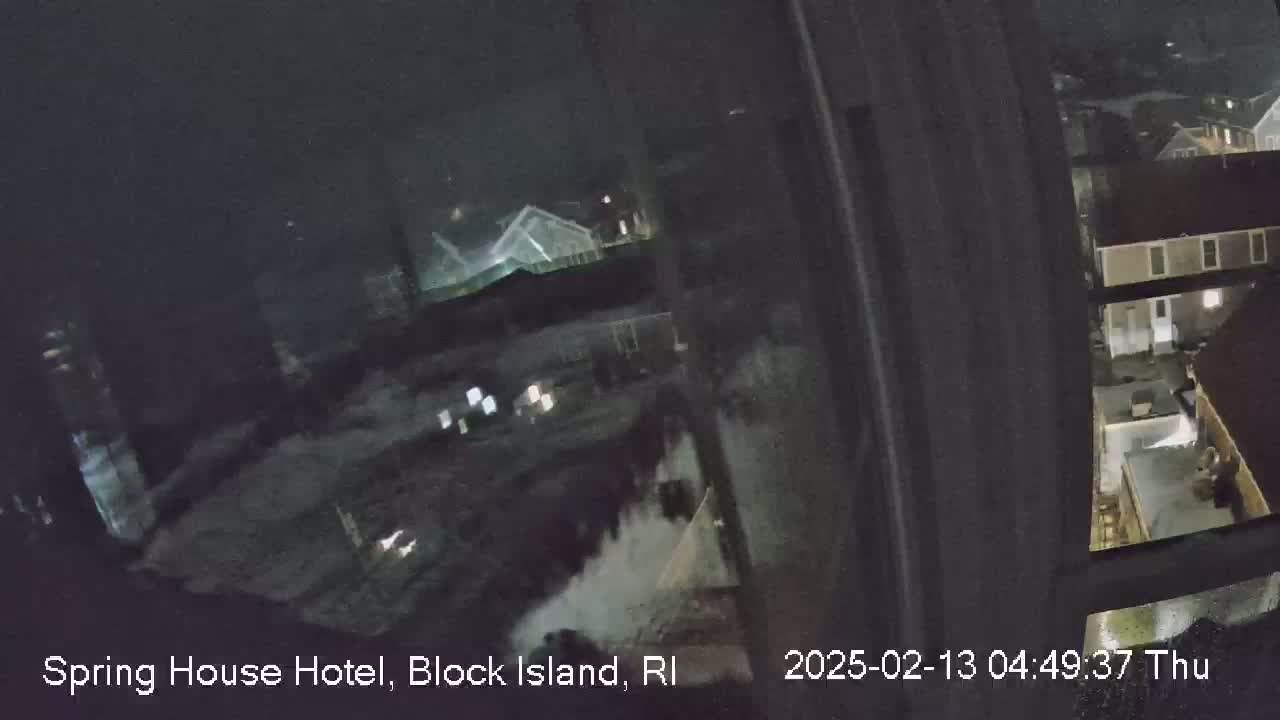 A nighttime, blurry view from a window shows a dark, snow-covered landscape with buildings and some lights.