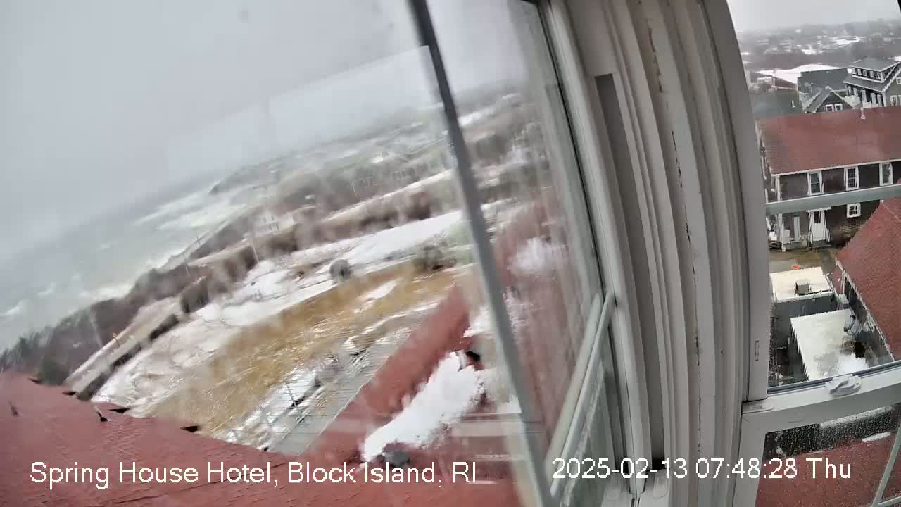 A snowy, stormy view of a coastline and buildings is seen through a window.