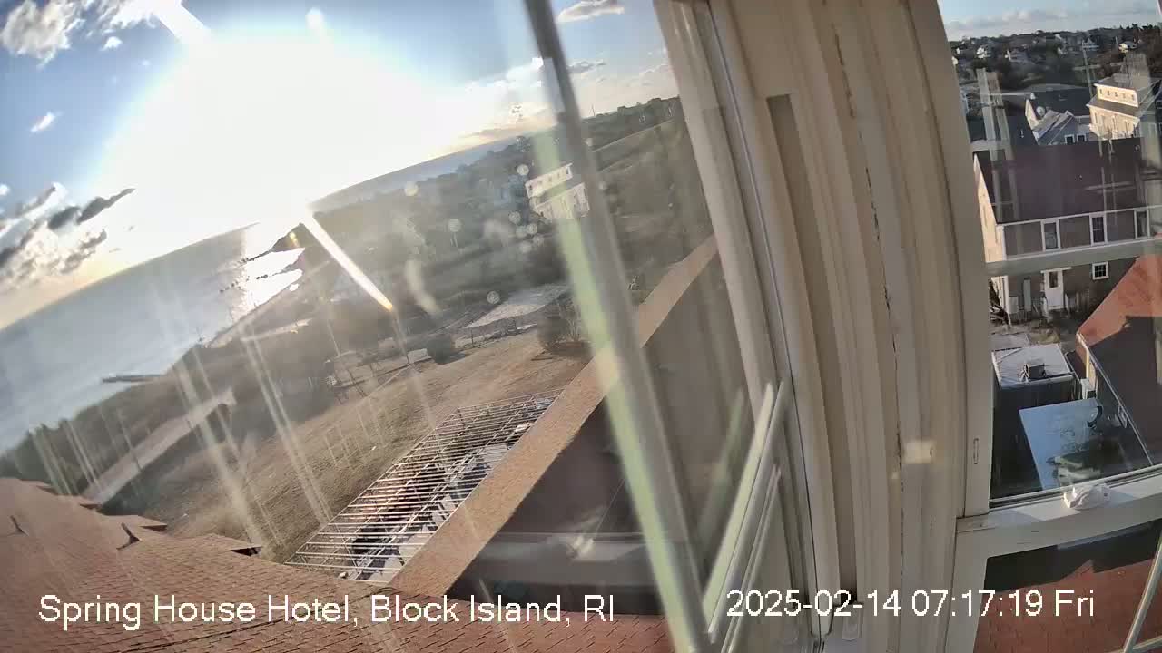 A view from a window shows a partly sunny, cold-looking day overlooking a coast, buildings, and a partially constructed structure.