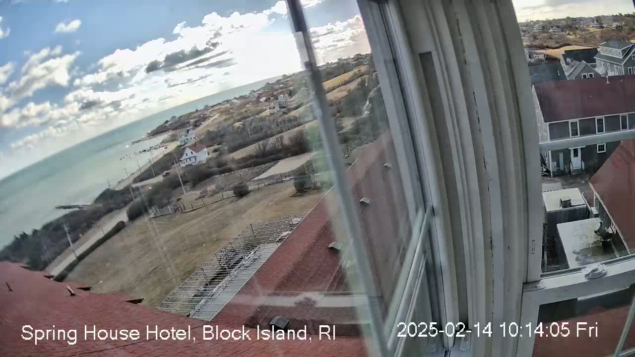 A partly cloudy day view of a coastline, buildings, and a  red roof from a window.