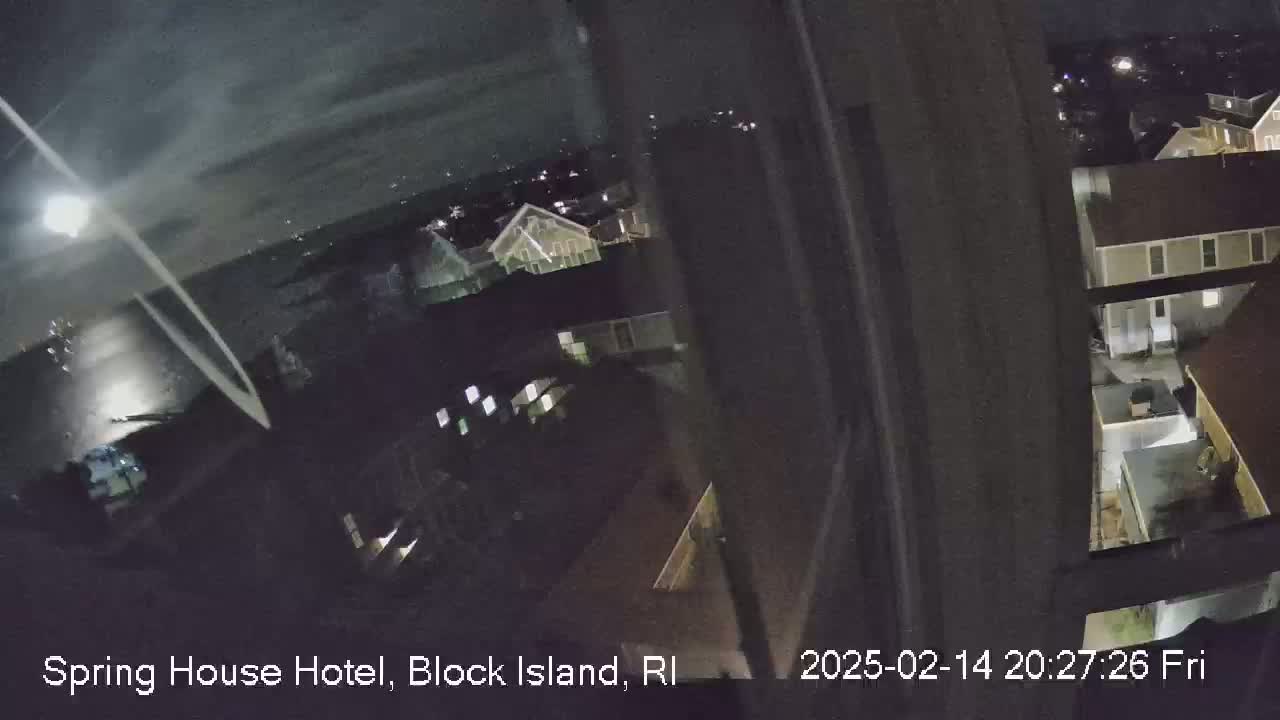 A nighttime, high-angle view through a window shows a dimly lit residential area with several buildings.