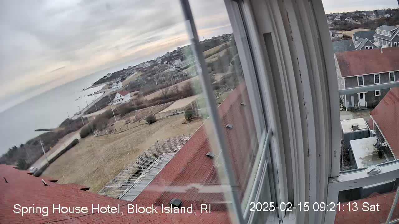 A view from a window shows a coastal town under an overcast sky, with a calm ocean in the background.