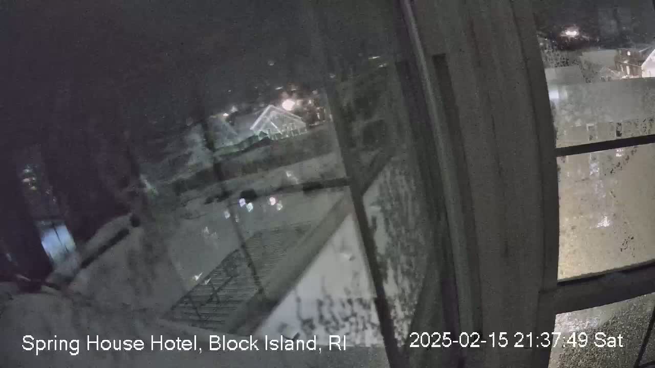 A nighttime view through a snow-covered window shows a dimly lit exterior with buildings and some lights.
