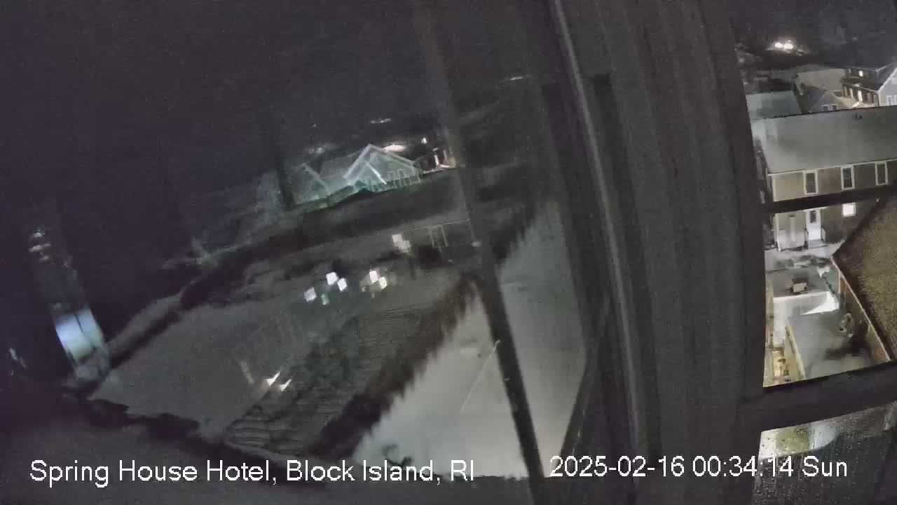 A nighttime view from a window shows snow-covered ground and buildings in a residential area.