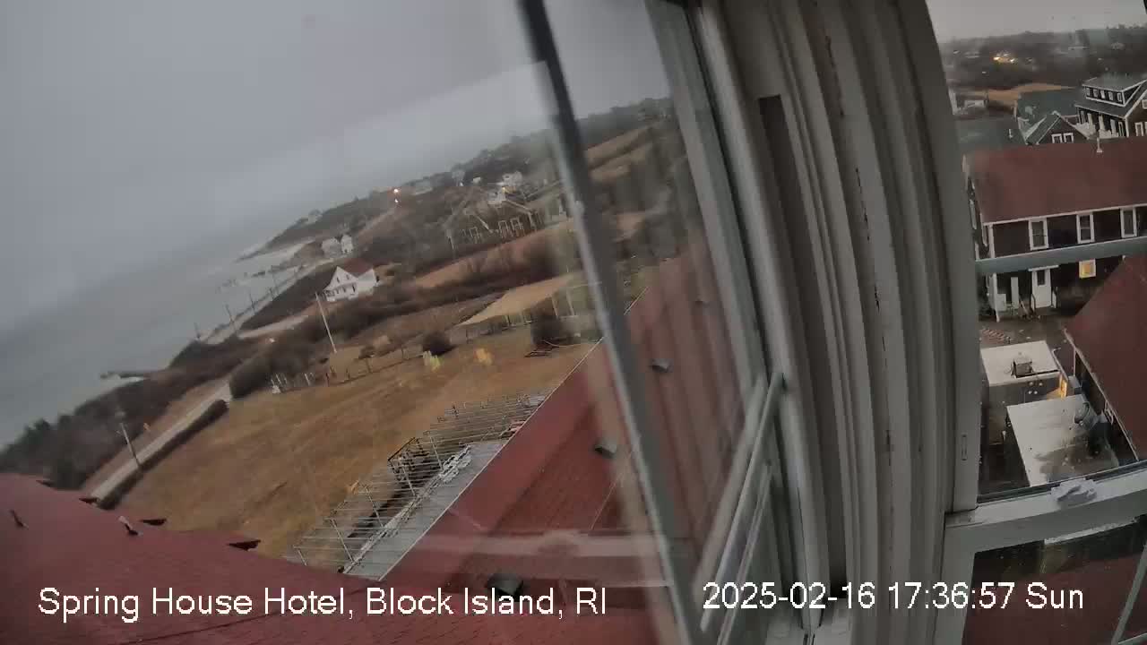 A view from a window shows a coastal town under an overcast sky, with a body of water visible in the distance.